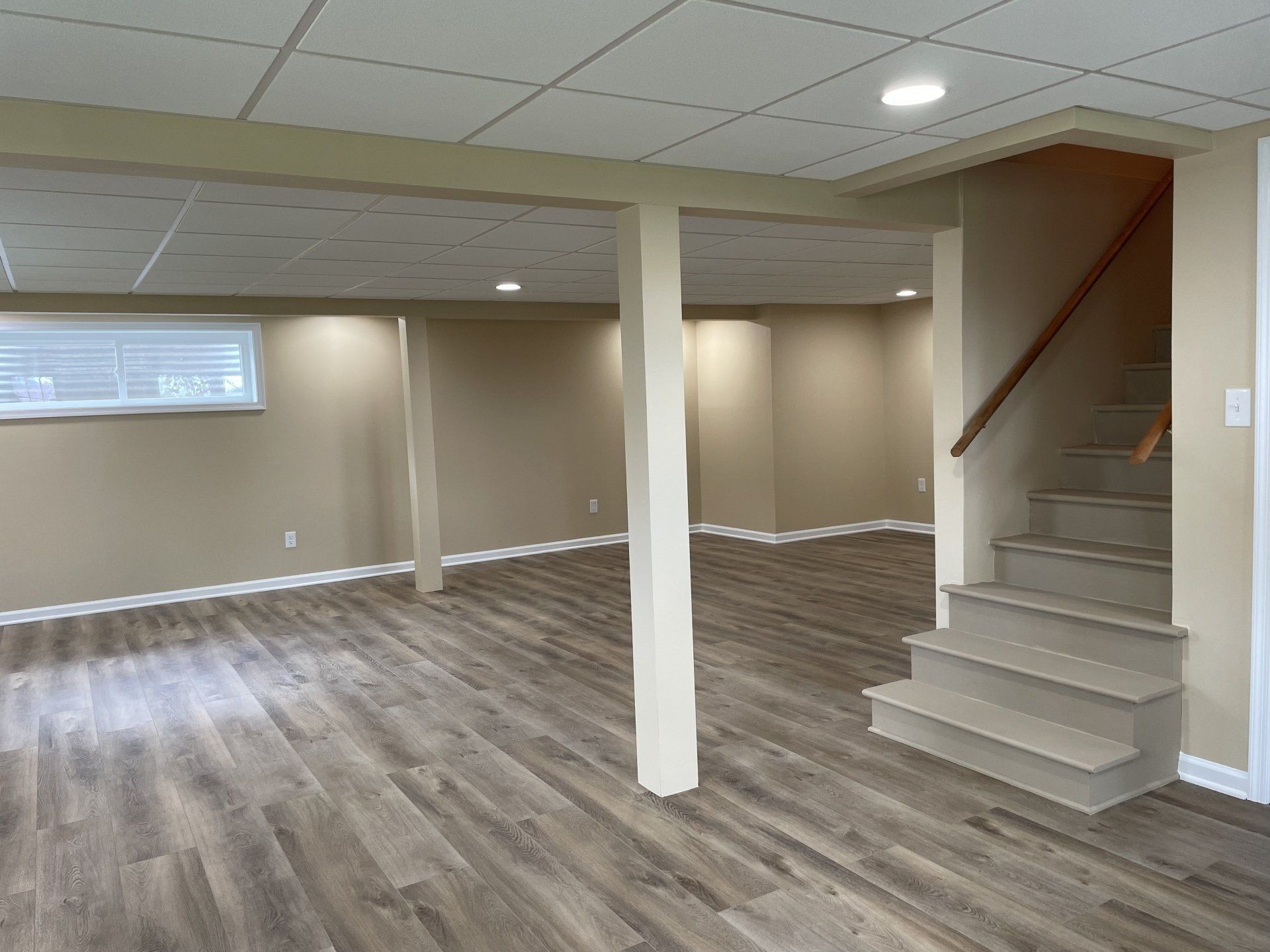 An empty basement with hardwood floors and a window.