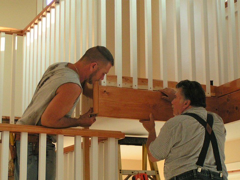 Two men are working on a wooden railing on a staircase.