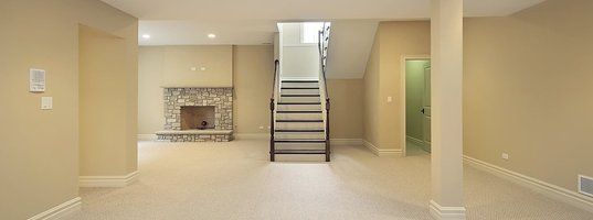 An empty basement with stairs leading up to the second floor and a fireplace.