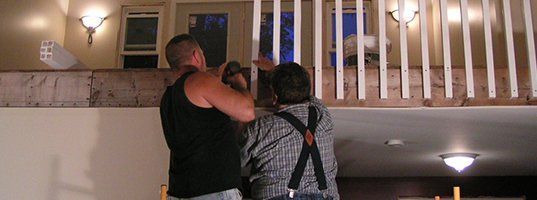 Two men are working on a railing in a room.