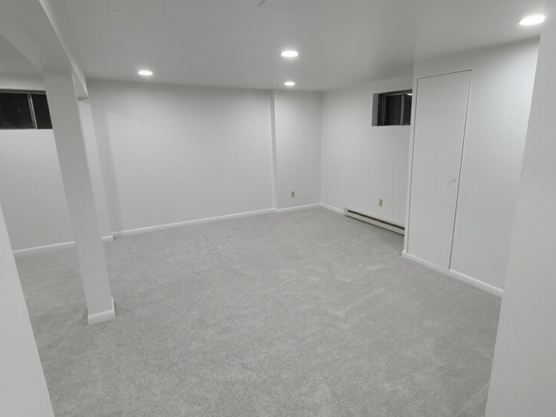 An empty basement with a carpeted floor and white walls.