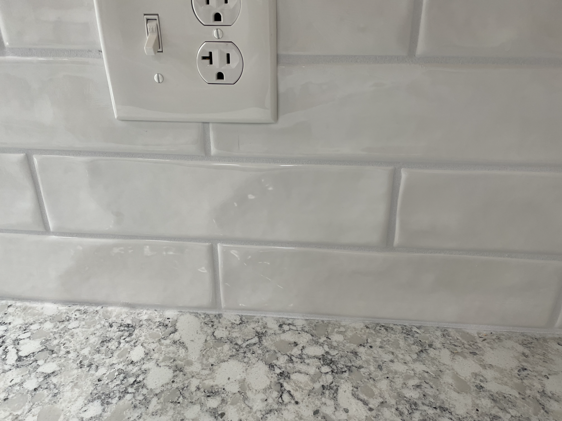 A white brick wall with a white electrical outlet and a light switch.