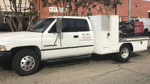White utility truck parked outdoors beside a brick building and trees