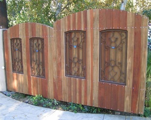 Wooden fence with four decorative metal-and-glass window panels along a sidewalk outdoors