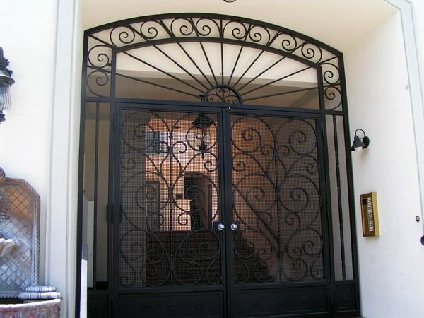 Black wrought-iron double gate with decorative scrollwork at a building entrance
