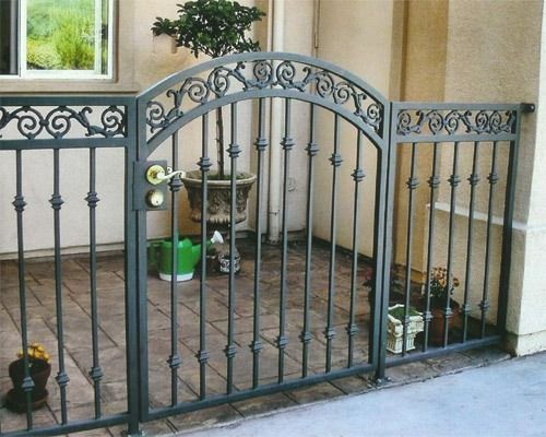 Decorative black metal garden gate and fence enclosing a small patio with potted plants