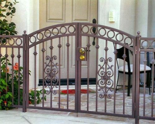 Brown wrought-iron gate with decorative arches in front of a house entrance and patio steps