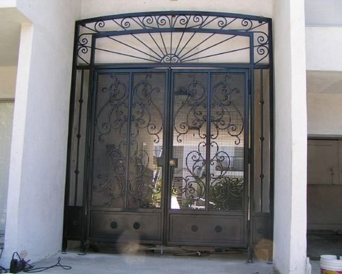 Black wrought-iron double gate with ornate scrollwork set in a white entryway.