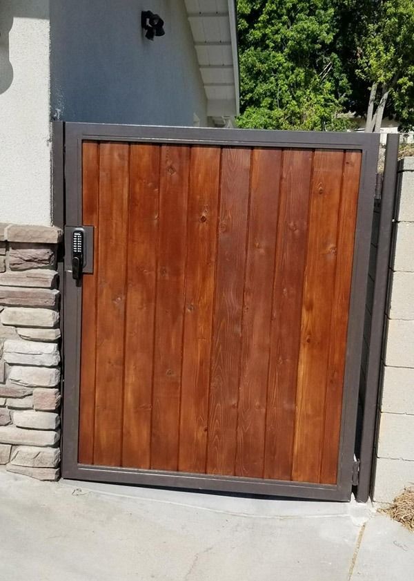Wooden front gate with dark gray frame set in a stone wall beside a driveway