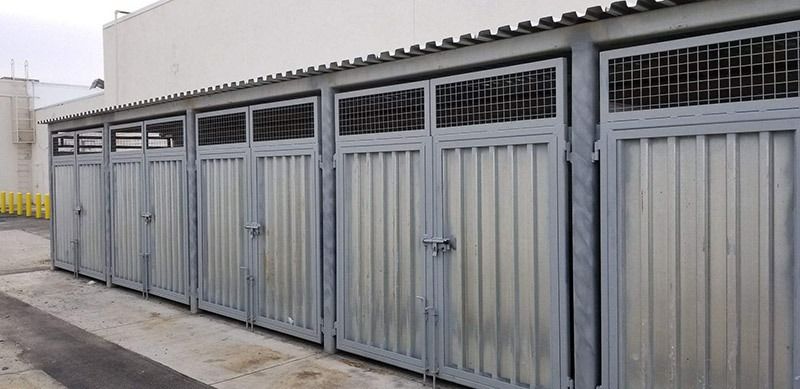 Row of gray metal storage lockers with vented tops along an outdoor industrial wall