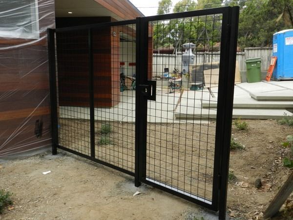 Black metal mesh gate beside a building under construction, with a latch in the center.