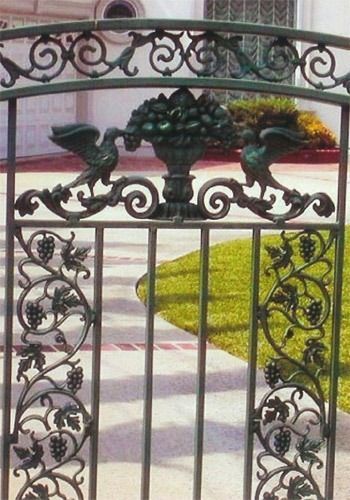 Decorative wrought-iron gate with birds and grape motif in front of a garden path