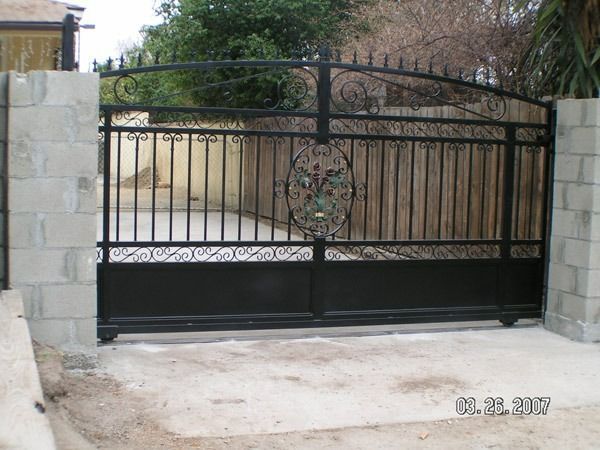 Closed black wrought-iron gate between stone pillars at a driveway entrance