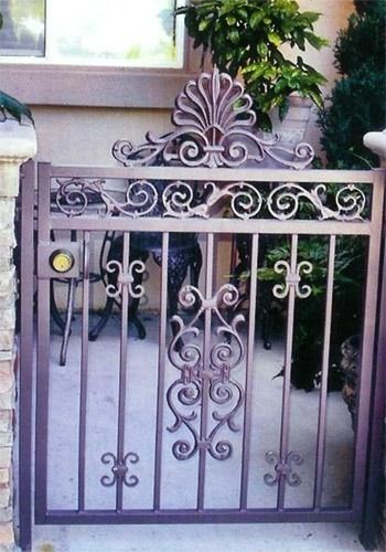 Decorative black metal garden gate with ornate scrollwork and a central floral design in front of a house
