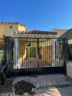 Front view of a yellow house with a black metal gate and blue sky above
