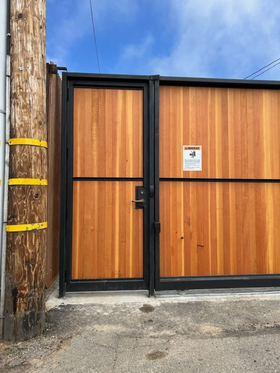 Wooden sliding gate with black metal frame beside a utility pole on a street.