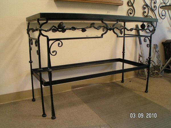 Black wrought-iron console table with glass top and lower shelf against a beige wall