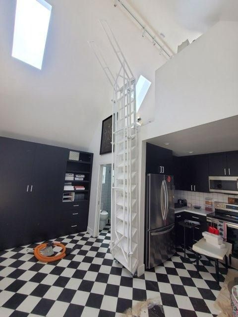 Modern kitchen with black-and-white checkered floor, dark cabinets, stainless fridge, and a spiral staircase