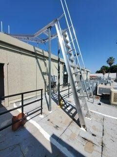 Worker on a rooftop ladder beside a beige building under a clear blue sky