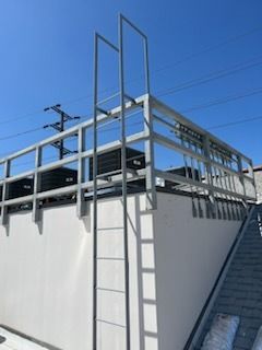 Rooftop walkway with metal railing and tall ladder against a white building under a blue sky