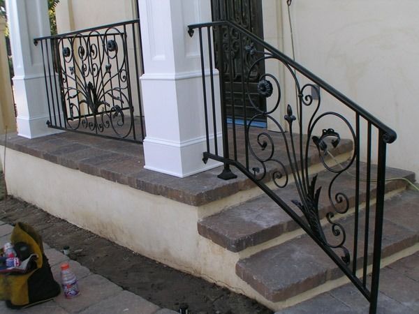 Front porch steps with black wrought-iron railing and white columns beside a doorway