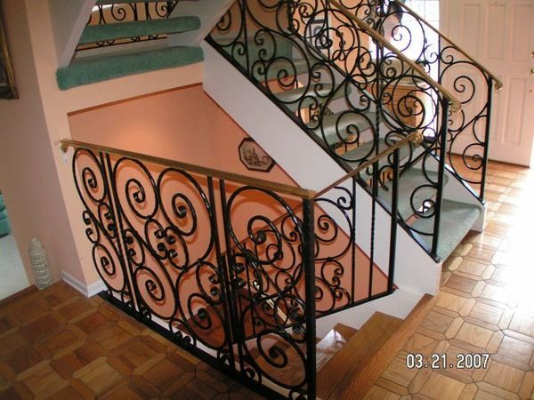 Indoor staircase with ornate black wrought-iron railings and tiled steps in a bright foyer