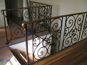 Staircase with ornate black wrought-iron railing and tiled floor in a hallway