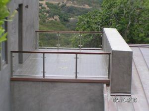 Concrete balcony with metal railing overlooking a green hillside, with a wooden beam and post in the foreground