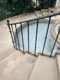 Concrete steps beside a small round pool with a black metal railing and trees beyond.