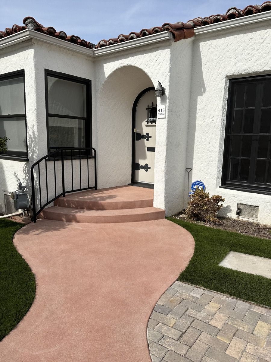 Front entrance of a white stucco house with arched doorway, curved red walkway, and black railings