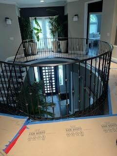 Interior balcony with black railings overlooking a stairwell and large windows in a modern home