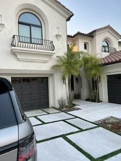 Modern white stucco house with arched windows, garage, palm trees, and a tiled driveway