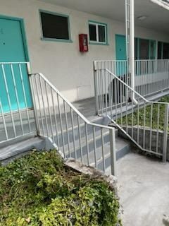 Accessible apartment walkway with a ramp, stairs, and white railings beside teal doors