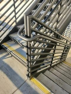Staircase landing with metal railings and yellow tactile paving on concrete steps