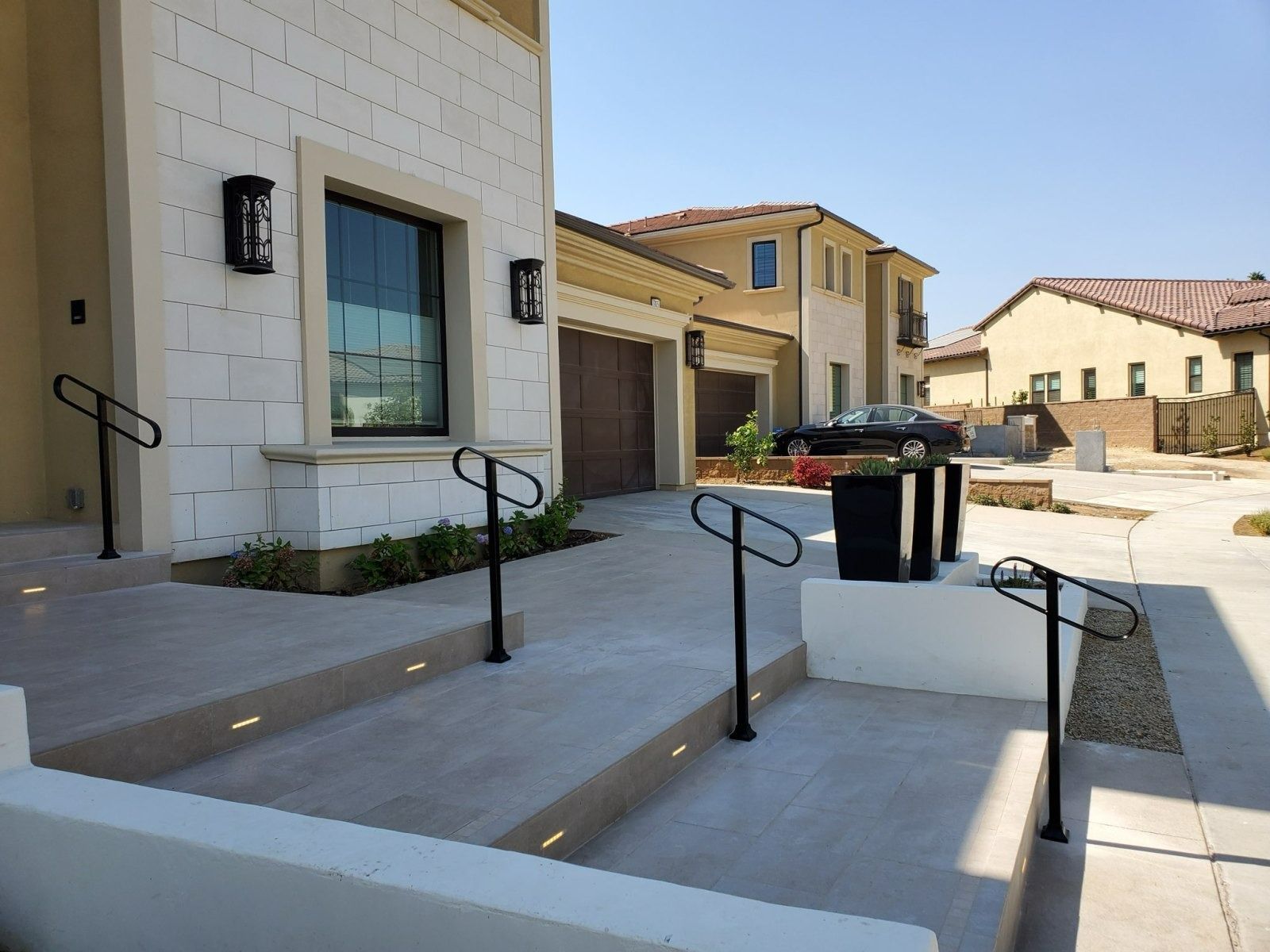 Accessible apartment entrance with ramps, handrails, and trash bins in a sunny residential courtyard