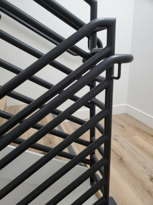 Black metal stair railing with diagonal bars beside a light wood floor and white wall