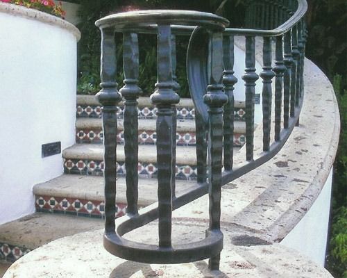 Curved outdoor staircase with patterned tiles and black wrought-iron railings