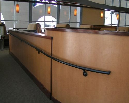 Wood-paneled office corridor with black handrails and pendant lights overlooking cubicle partitions.