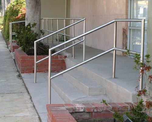 Concrete ramp with metal handrails beside steps and a sidewalk outside a building