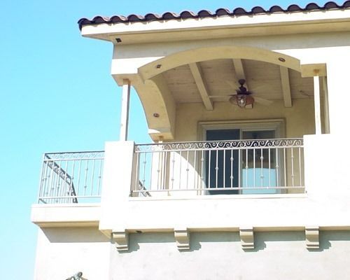 Balcony with white railings and cream columns under a tiled roof against a blue sky