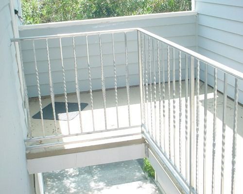 White metal balcony railing over a small outdoor landing with light siding and a shaded floor area