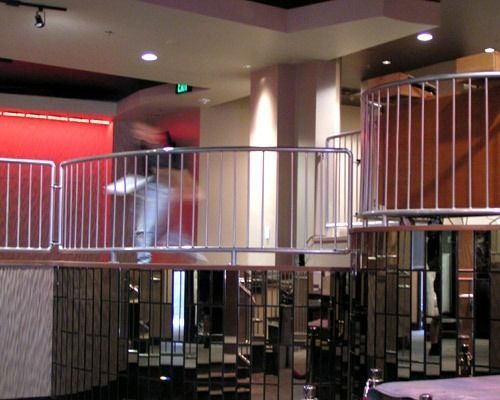 Indoor balcony with metal railings and a blurred person walking past a red wall