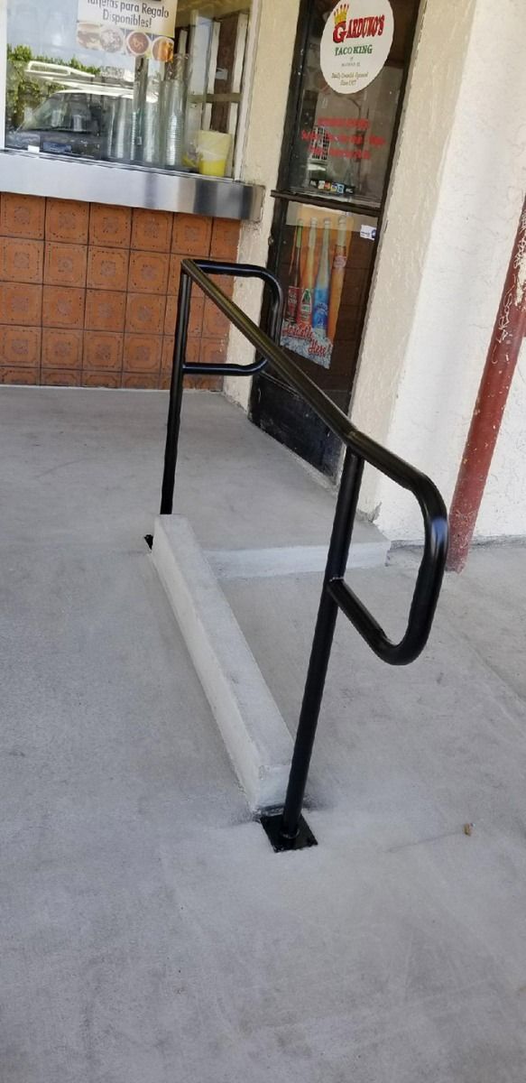 Store entrance with a metal handrail and a low curb ramp on a concrete walkway.