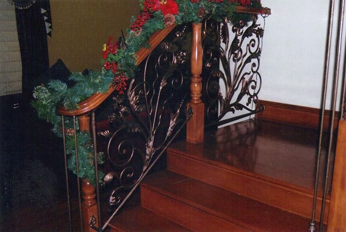 Decorated wooden staircase with ornate black wrought-iron railing and red-green garland