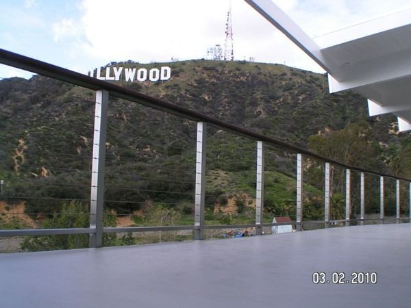 Hollywood sign on a hillside viewed from a walkway with railings and a cloudy sky