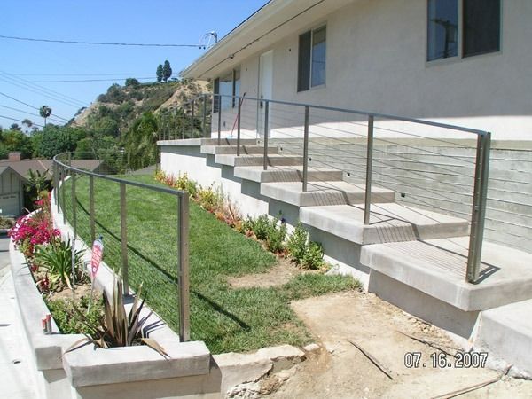 House exterior with a tiled ramp and stairs, metal handrails, and a landscaped slope beside a sidewalk