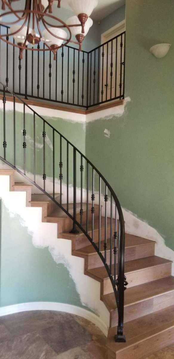 Curved staircase with black iron railing and green walls in a house interior