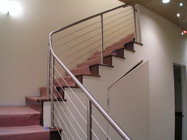 Curved indoor staircase with pink carpeted steps, silver railing, and wall-mounted lights