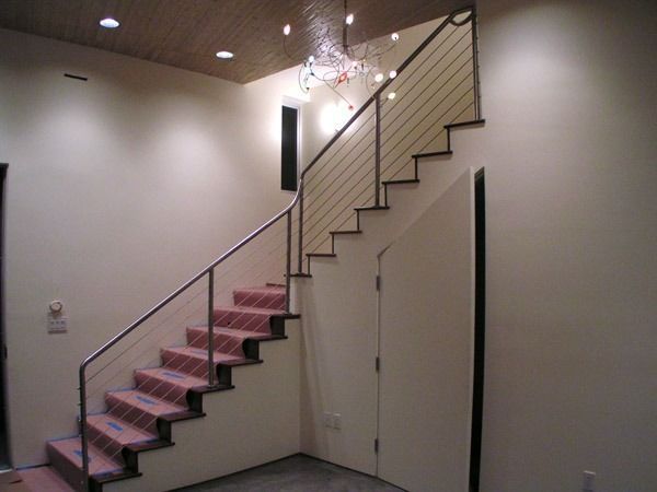 Interior staircase with pink carpeted steps, black railings, and a chandelier in a beige hallway
