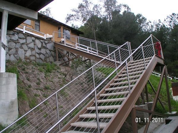 Outdoor stairway with metal railings ascending a steep hillside beside a stone retaining wall